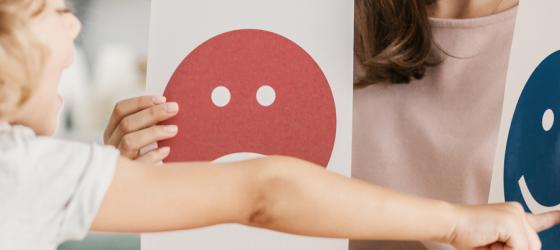 Una bimba indica con la mano l'emozione che sta provando: una faccia sorridente